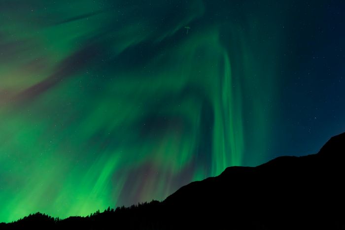 Aurora boreală verde strălucind pe cerul nopții deasupra munților